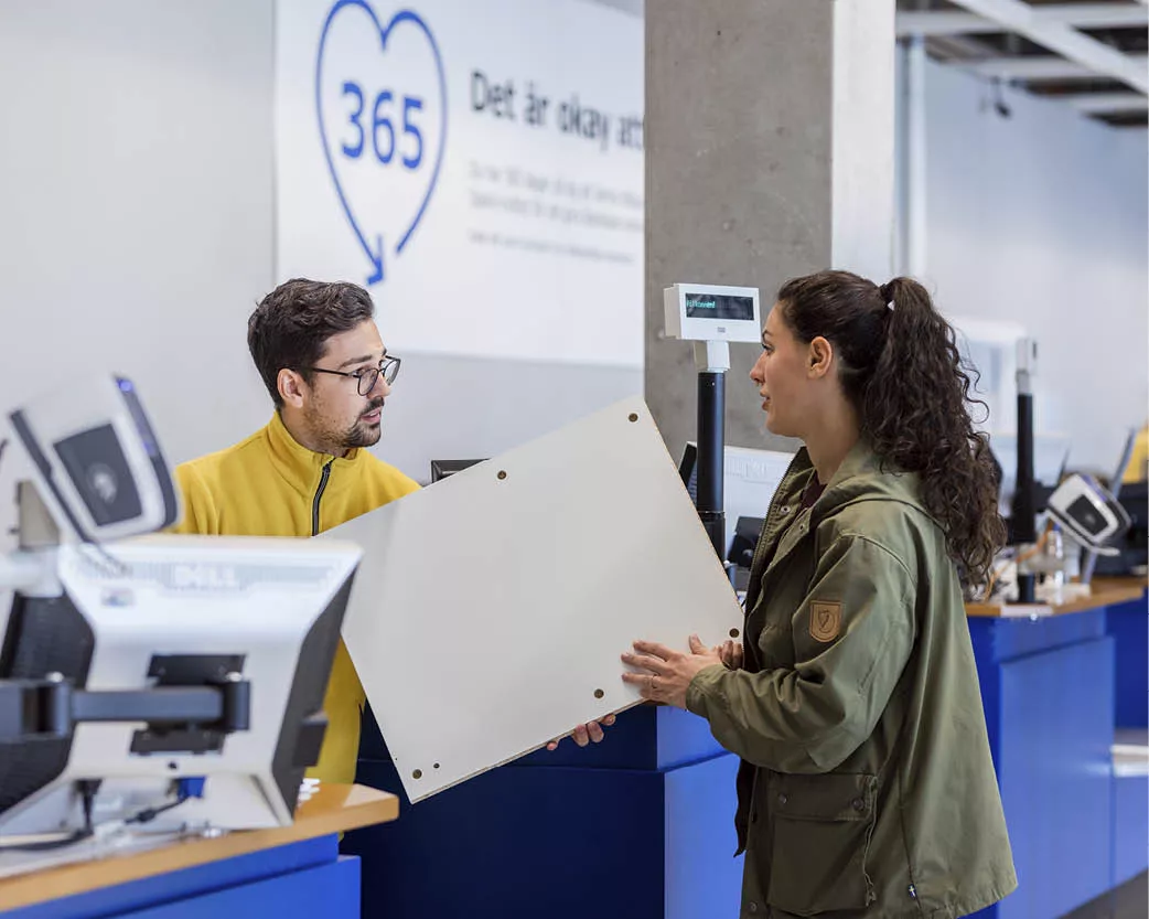 Customer handing a white furniture panel to an employee at a store returns counter.