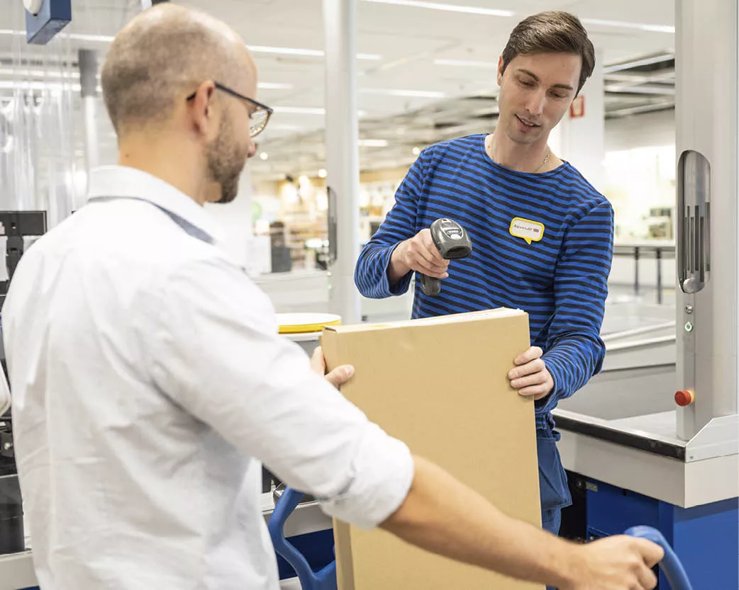 Cajero escaneando una caja de cartón grande sostenida por un cliente en una tienda.