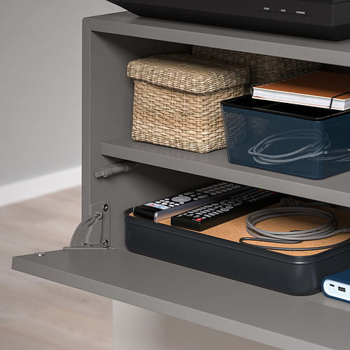 Almacenamiento montado en la pared con frente abatible para controles remotos y cables.