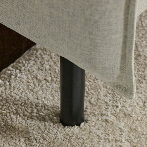 Patas de sofá de metal negro sobre una alfombra beige texturizada.