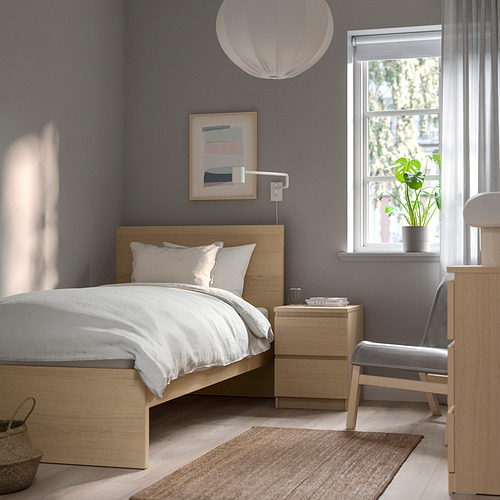 Dormitorio minimalista con temática marrón y blanco. Cama MALM, pared oscura, lámpara colgante, plantas y alfombra.