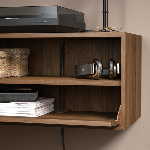Estante de pared de madera con puerta abatible que muestra auriculares y libros. Acabado en tono medio con soportes negros.