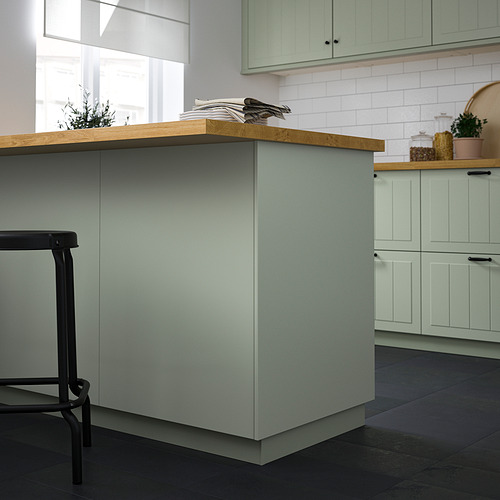 Cocina moderna con un gran panel de cubierta STENSUND verde claro, encimera de madera, taburete negro, salpicadero de azulejos blancos y plantas. El tamaño de los paneles es prominente.