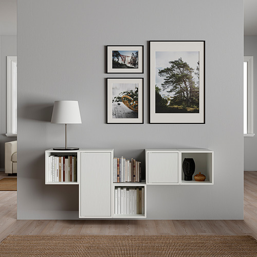 Sala de estar moderna con pared gris con unidad de almacenamiento blanca que sostiene libros y una lámpara, rematada con tres fotos de la naturaleza enmarcadas.