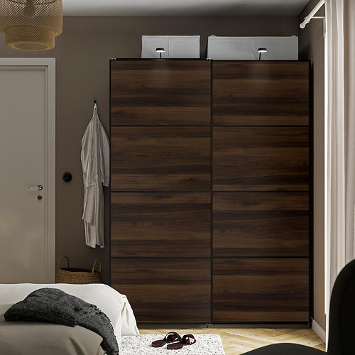 Dormitorio con gran armario MEHAMN marrón oscuro, puertas correderas, cama gris, ropa colgada, cesta.