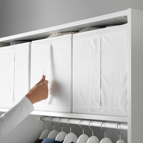 Persona organizando cajas de almacenamiento SKUBB en un armario, destacando la característica funcional de la caja con asa.