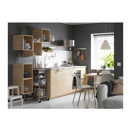 Cocina moderna con gabinetes de madera, electrodomésticos blancos y sofá gris. Estantes abiertos, platos de exhibición. Taburete, sillas de madera, ventana y planta.