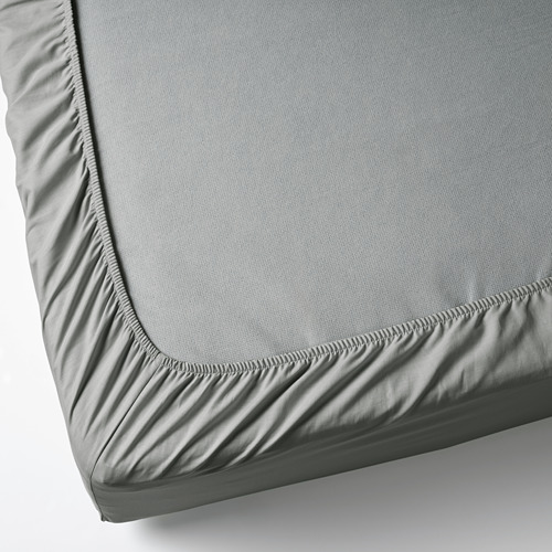 Una sábana ajustable de algodón gris sobre un colchón blanco, los bordes elásticos garantizan un ajuste seguro.
