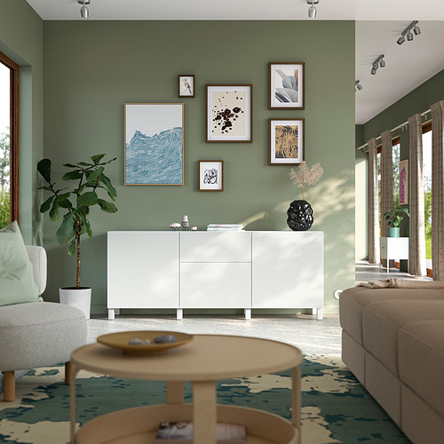 Salón moderno con armario blanco BESTÅ . Pared de galería, planta, mesa de centro y sofá. Paredes pintadas de verde. Adaptado para baja visión.