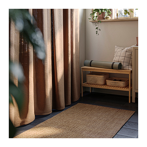 Espacio interior relajante con alfombra LYDERSHOLM beige, banco de madera, colchoneta de yoga y ventana con cortinas.