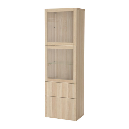 Un armario de almacenaje de roble claro BESTÅ de ikea con puertas y cajones de cristal. Es alto, rectangular y tiene un diseño minimalista.