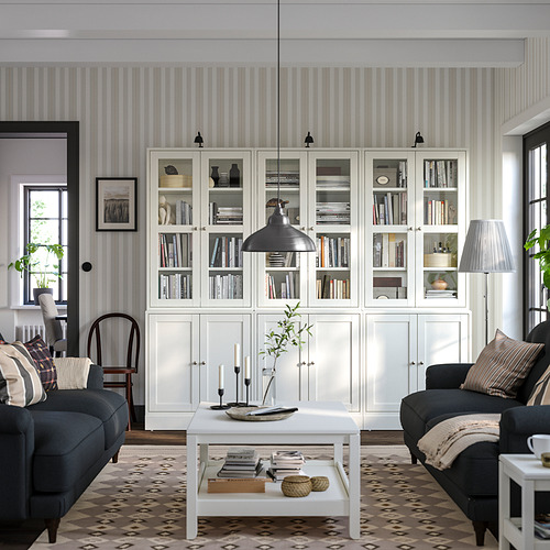 Nueva sala de estar: estanterías de pino blanco HAVSTA, sofás grises, lámpara colgante negra, alfombra estampada, mesa de centro con decoración y almohadas.