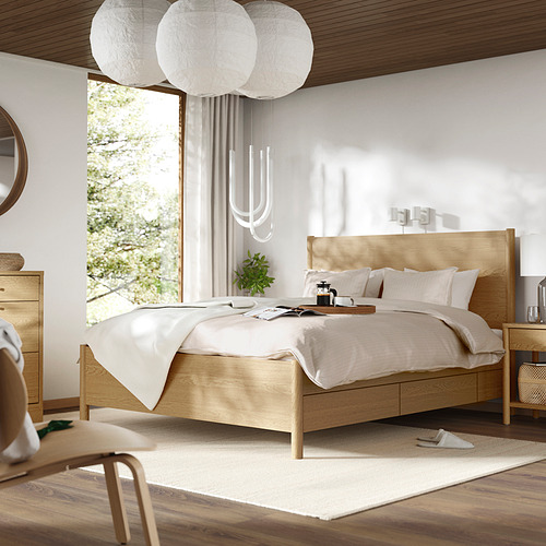 Dormitorio minimalista con cama TONSTAD de madera clara, ropa de cama blanca, lámparas colgantes y un gran ventanal.