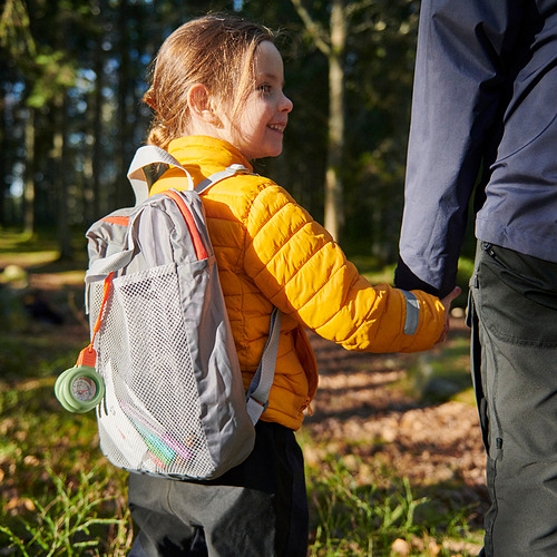 Un niño con una chaqueta amarilla lleva una mochila MAJBAGGE gris claro con bolsillos de malla y una brújula.