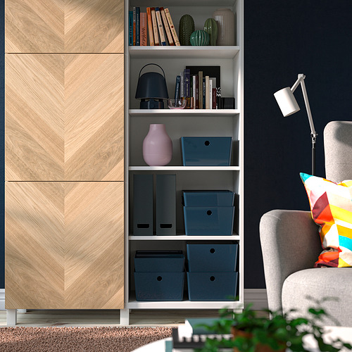 Salón moderno con caja azul de KUGGIS en la estantería entre libros y decoración, panel de madera clara, pared oscura, sillón acogedor con cojines de colores.