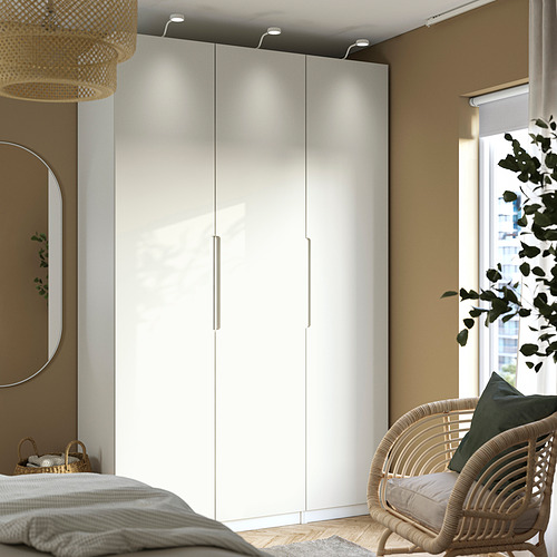 Un dormitorio moderno con una puerta de armario TONSTAD en color blanco roto, más alta que la silla de mimbre cercana, con un diseño elegante y bordes suaves.