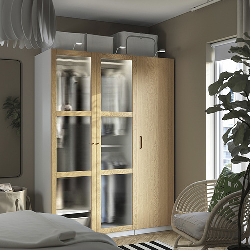 Dormitorio moderno con armario de madera clara TONSTAD, silla y plantas.