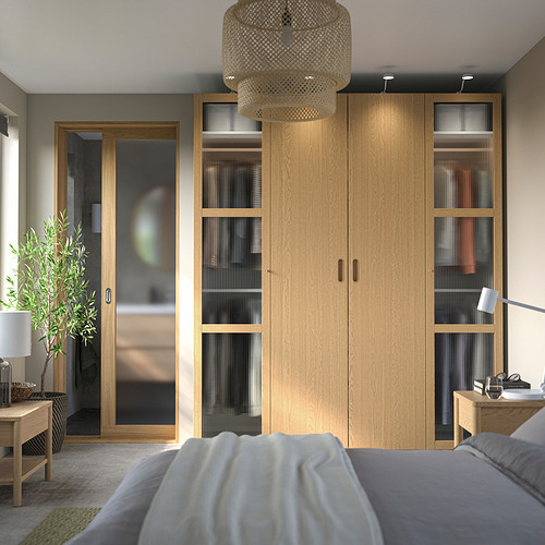 Dormitorio moderno con gran armario de madera PAX; estanterías y cajones, flanqueados por mesitas de noche con lámparas. Iluminación suave desde el colgante tejido de arriba.