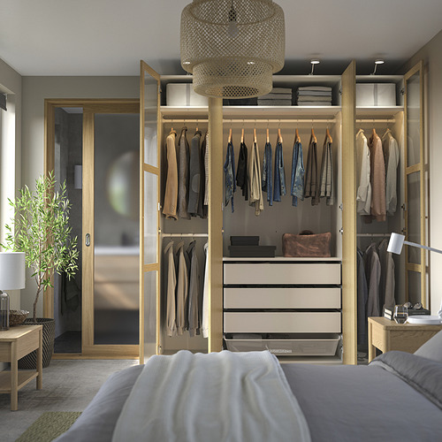 Armario moderno de madera con puertas de vidrio, iluminación y cama con sábanas grises/blancas.