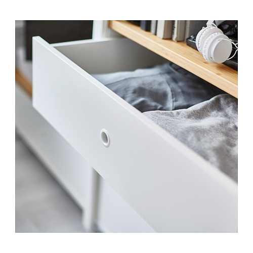 Cajón de almacenamiento abierto en metal blanco y bambú, parcialmente relleno de tela gris doblada.