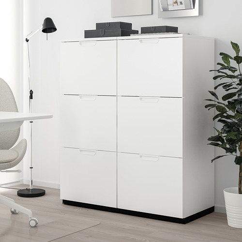 Mueble de almacenaje GALANT blanco con cajones, alto y de diseño moderno, junto al escritorio, la silla y la planta.