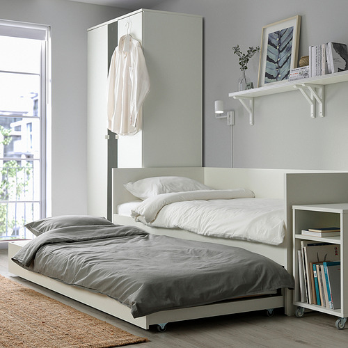 Dormitorio moderno con un sofá cama blanco con una cama nido debajo, que proporciona espacio adicional para dormir. Decorado de forma sencilla con libros y una planta.
