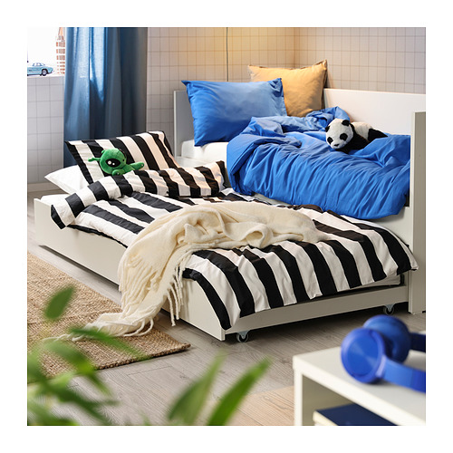 Cama nido blanca, rayas blancas y negras, detalles en azul; panda, juguetes de lagarto; Habitación luminosa, plantas.