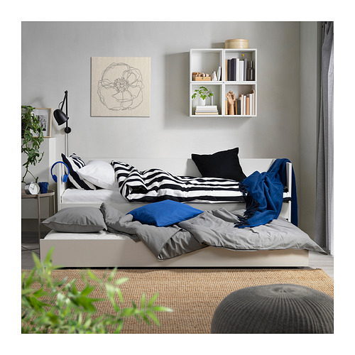 Dormitorio moderno con sofá cama VIHALS, nido, ropa de cama en blanco y negro, almohadas grises y azules y estantes de pared decorados.