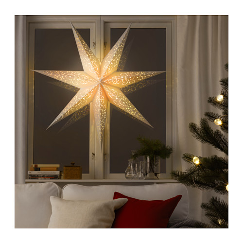 Acogedora lámpara estrella de interior en la ventana, iluminada con luz cálida, combinada con una decoración navideña como un árbol y ramas.