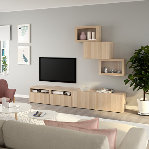 Mueble de televisión BESTÅ de roble con estantes y armarios, arte minimalista, plantas, pasteles. Sofá beige con almohadas rosas y mesa de centro blanca.