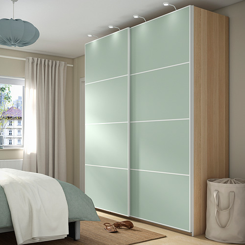 Dormitorio moderno con armario alto PAX verde menta y molduras de madera clara. Incluye cesta de lavandería, se coloca cerca de la ventana.