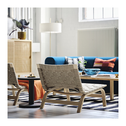 Sala de estar moderna con sillón de madera clara, asiento de lino tejido, sofá azul y alfombra a rayas.