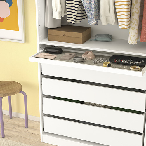 Cómoda blanca con cajones, bandeja superior para bolsos, cajas y accesorios, colocada contra la pared amarilla.