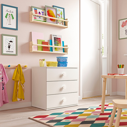 Habitación infantil con cómoda blanca de 3 cajones, estantes llenos de juguetes, paredes rosas.
