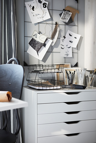 Moderna configuración de oficina con tablero de notas SÖSDALA blanco que muestra notas y fotos. Incluye cesta de alambre metálico con herramientas de escritura sobre un escritorio blanco.