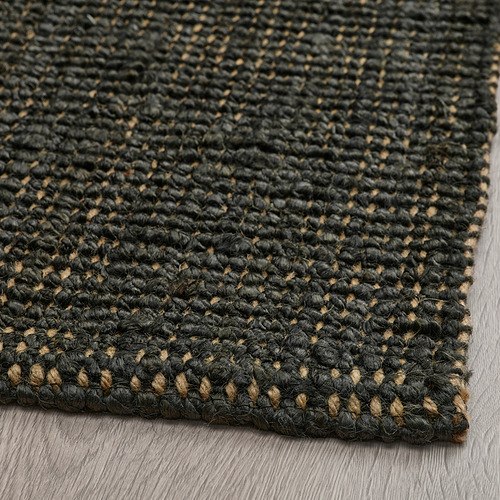 Alfombra de yute negro texturizado con motas de fibra natural, que muestra artesanía de alta calidad.