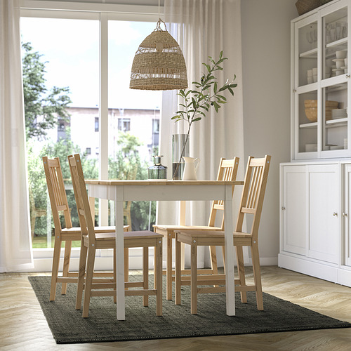 Comedor luminoso con mesa de madera clara y cuatro sillas, alfombra de yute LANDBANA verde oscuro, gran ventanal, armario blanco, lámpara colgante.
