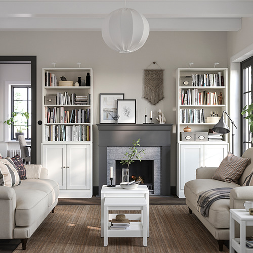 Sala de estar moderna con unidades de almacenamiento HAVSTA blancas, sofás gris claro, chimenea con marco negro y decoración neutra.