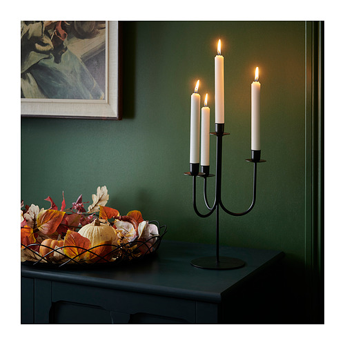 Tres velas encendidas en un candelabro negro junto a un cuenco de hojas de otoño.