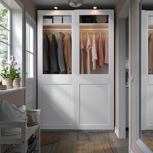 Armario blanco PAX con puertas de cristal, ropa y plantas.