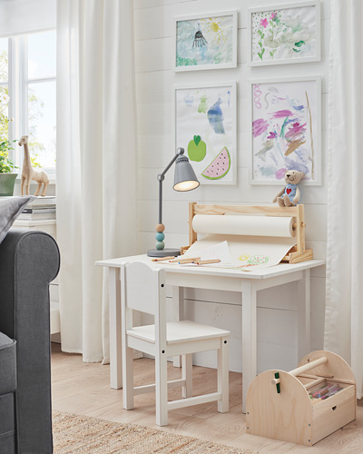 Brillante configuración de escritorio para niños con escritorio FISKBO blanco, silla y baúl de juguetes de madera. Colorido arte infantil en las paredes, lámpara gris y decoración de jirafas.