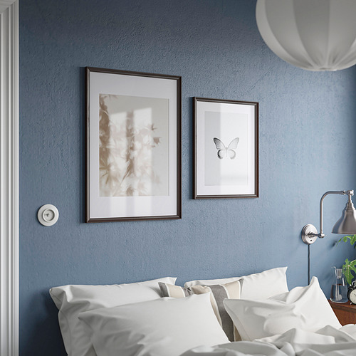 Reloj analógico encima de la cama, blanco con números negros. Dos marcos: abstracto, mariposa. Cama con almohadas blancas, paredes azules.