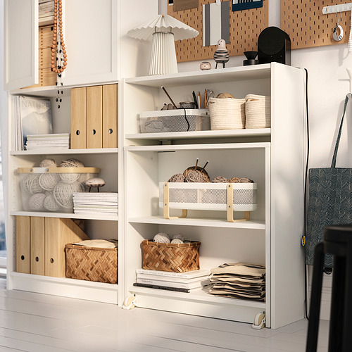 Librería blanca BILLY con mesa plegable, almacenamiento abierto y cerrado, exhibiendo hilo, libros, decoración y cestas. Diseño estable y anclado a la pared.