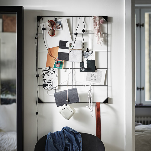 Tablero de notas moderno con clips negros muestra fotos y notas en una pared blanca.