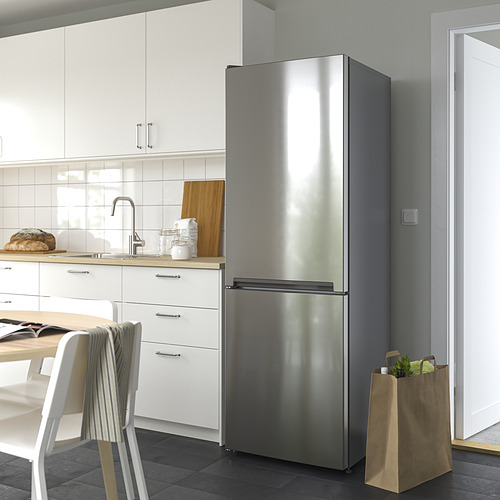 Cocina moderna con nevera de doble puerta de acero inoxidable VINDÅS, más grande que las sillas y armarios cercanos, con un diseño elegante y estantes de cristal.