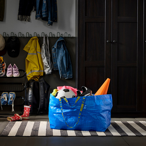 Bolso azul FRAKTA de ikea, relleno de ropa deportiva, sobre una alfombra a rayas.