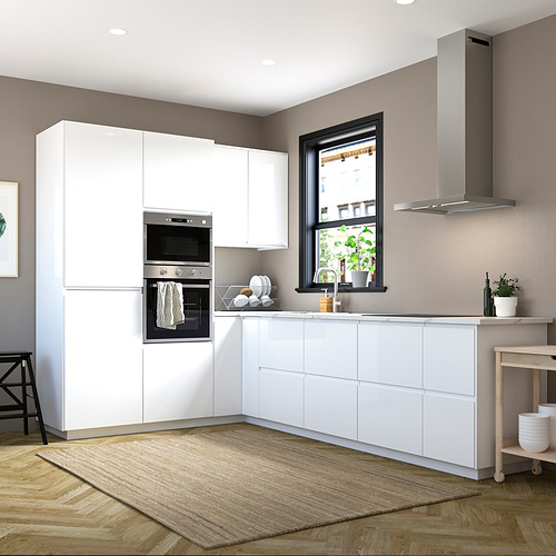 Cocina moderna con gabinetes blancos de alto brillo y manijas integradas, electrodomésticos de acero inoxidable, ventana grande, piso de madera y alfombra beige.