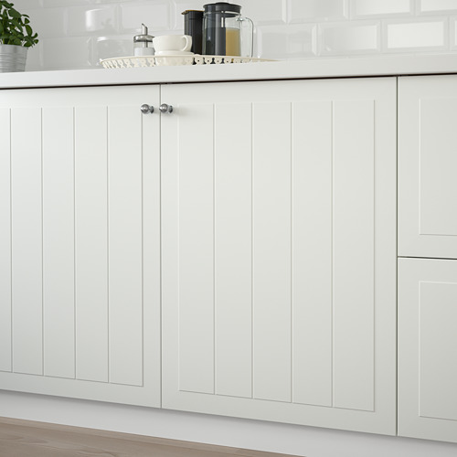 Mueble de cocina blanco con paneles ranurados, dos manijas cromadas y encimera con cafetera y tazas.