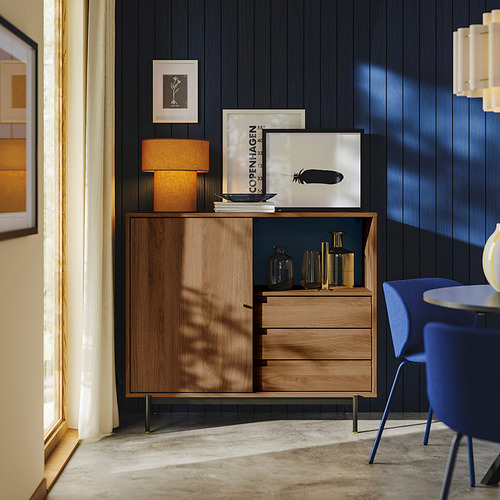 Mueble de nogal con patas negras, pomos de latón y puertas correderas junto a una silla azul.