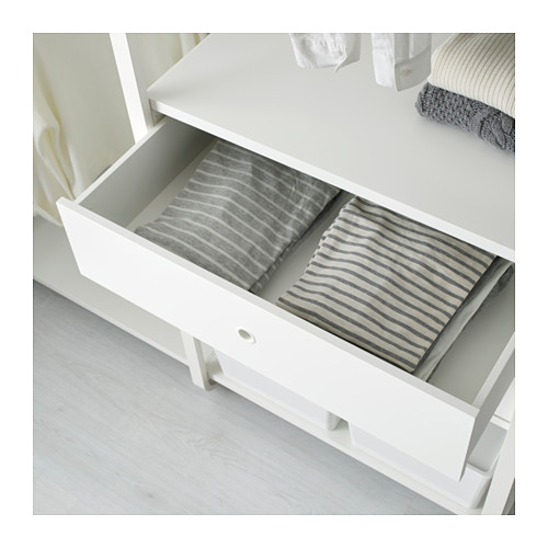 Una cómoda blanca con un cajón abierto que muestra ropa a rayas cuidadosamente doblada.